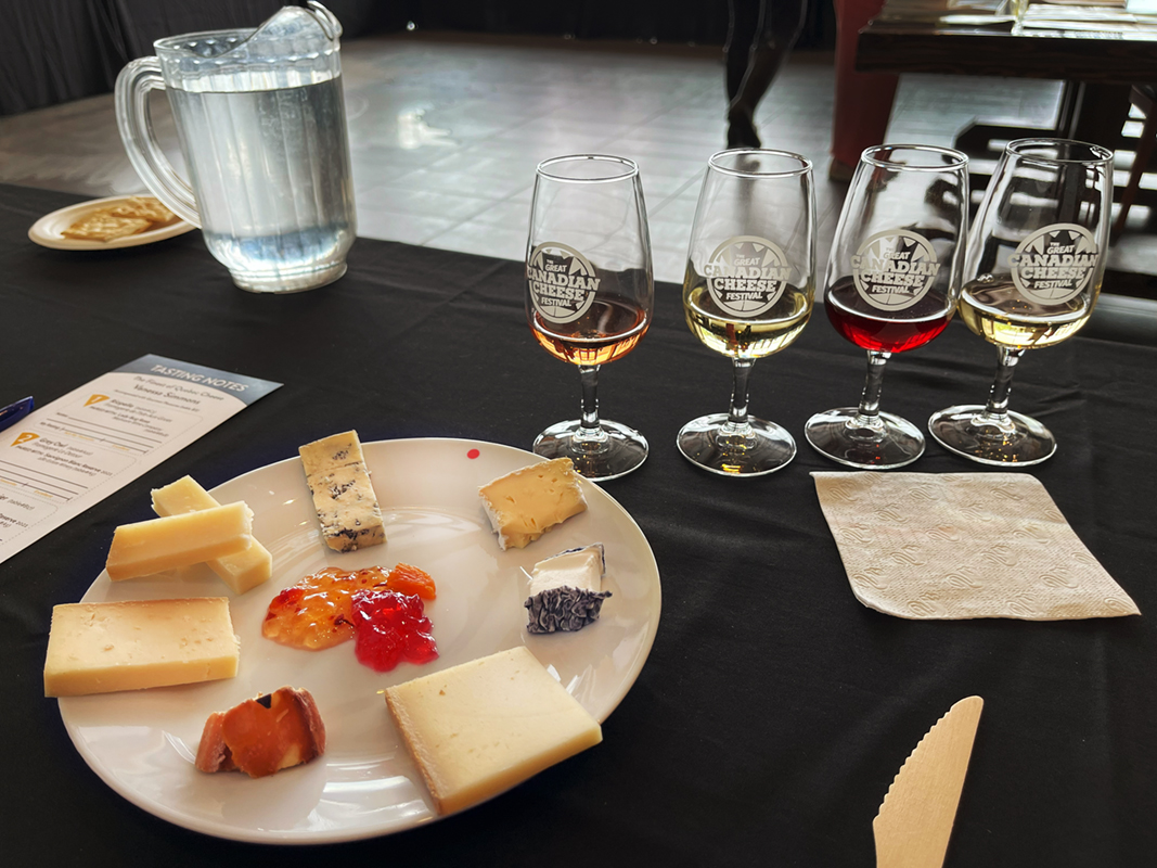 Tutored tasting setup at the Great Canadian Cheese Festival with plate of cheese, and branded glassware that reads "Great Canadian Cheese Festival"