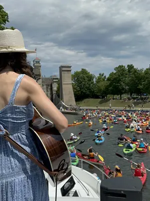 Woman playing a guitar on a larger boat while kayaks paddle up to Lock 21 - Peterborough Lift Lock.
