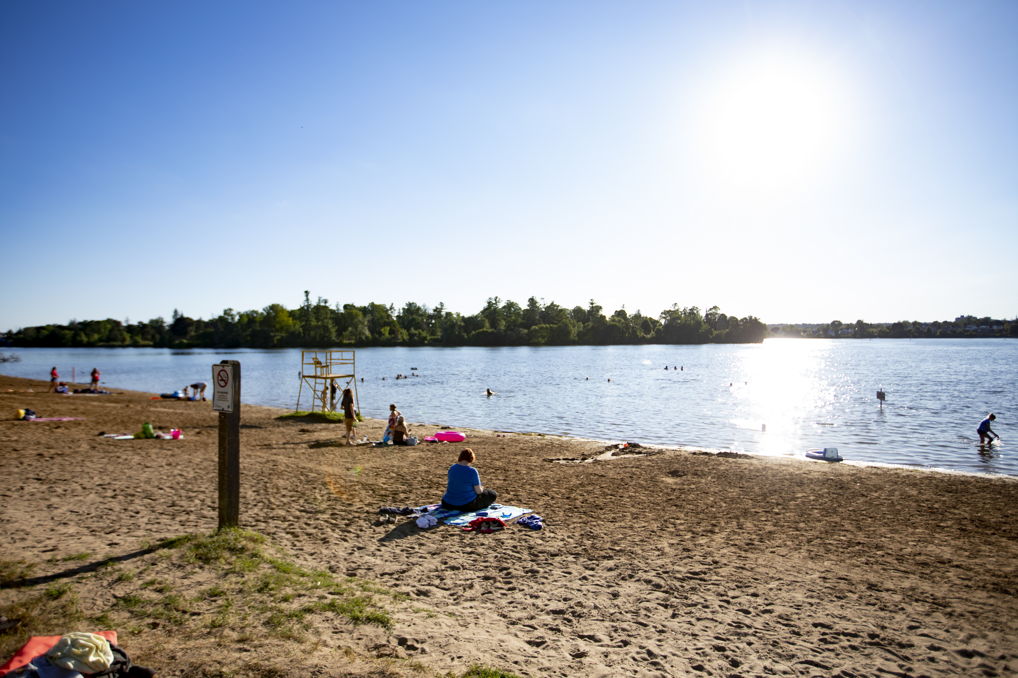 People spread out sitting on Beavermead Beach sitting in the sand and swimming in Little Lake.
