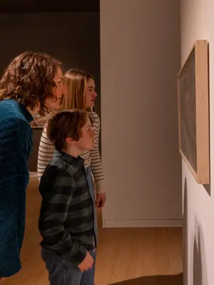 A family looking closely at a large painting in a large white gallery space.